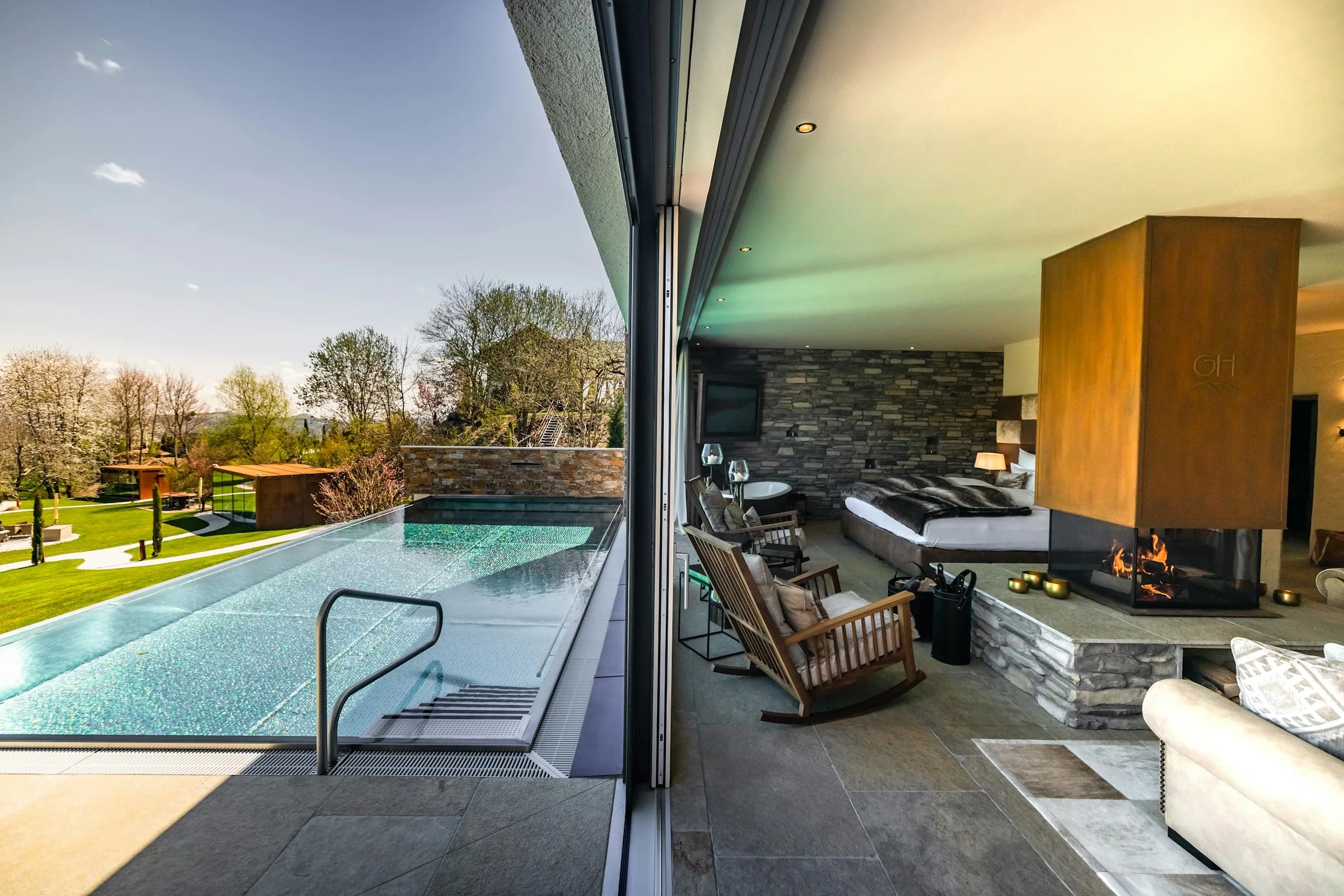 A pool and timber deck opening straight into a lounge with a stone fireplace