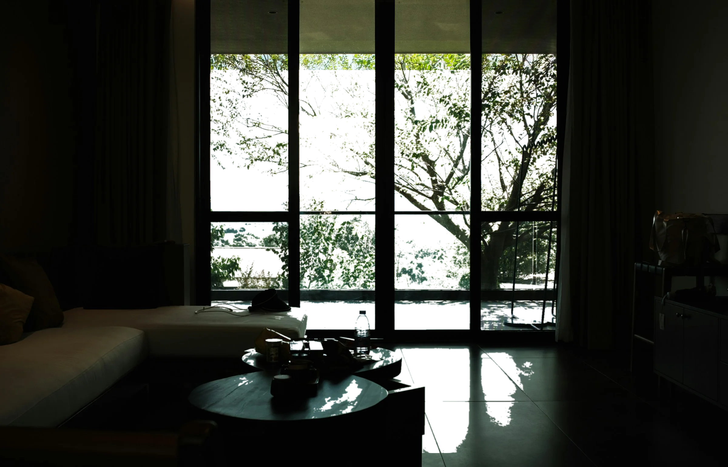 An unlit room with tall black window frames, mist moving across the ridge outside